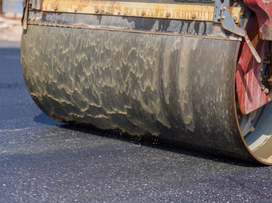 A steamroller is rolling over some relatively fresh black asphalt. It's helping to roll it out and keep it flat.