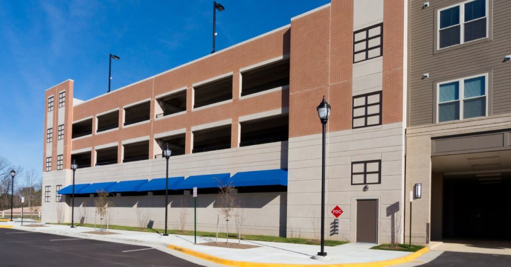 The exterior of a red brick parking garage. There are a few empty parking spots out front and the road is very clean.