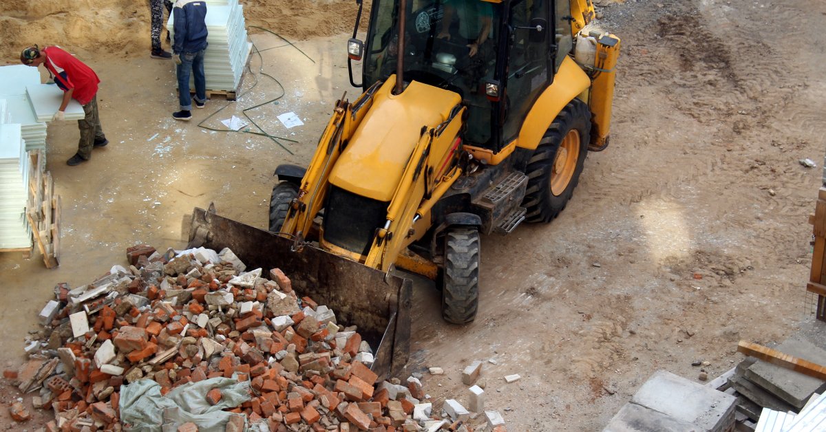 An overhead view of a construction site. A large yellow tractor uses a bucket to clear aside debris.