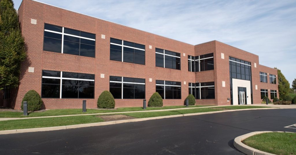 A large asphalt road is in front of a red brick commercial building. The pavement is in excellent condition.