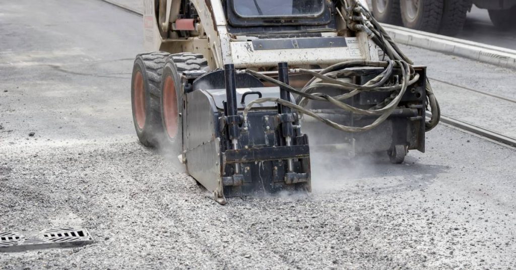 An asphalt grinder is going along a paved road and grinding up the top layer for milling purposes.