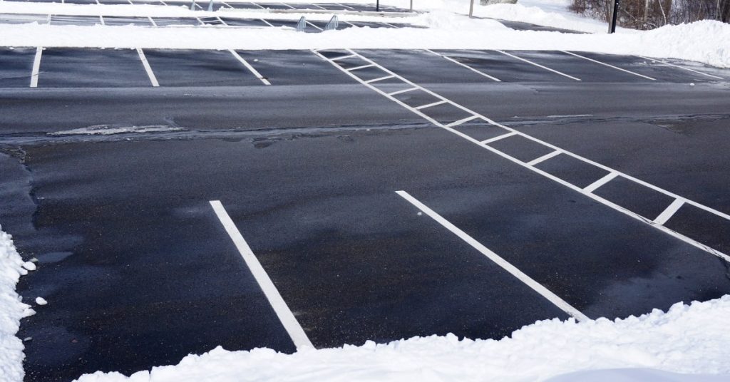 An empty parking lot with clear white lines. There's a lot of snow, but all of it has been pushed off to the sides of medians.