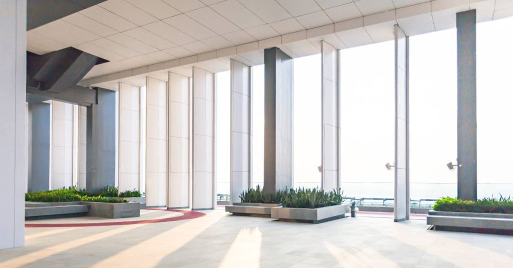 Interior of a commercial property building with several tall pane windows. Throughout the room are potted shrubs.