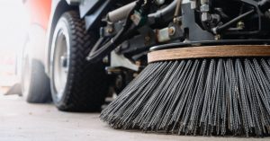 Close-up of an industrial street sweeper. There is a large circular brush attachment with nylon threads.