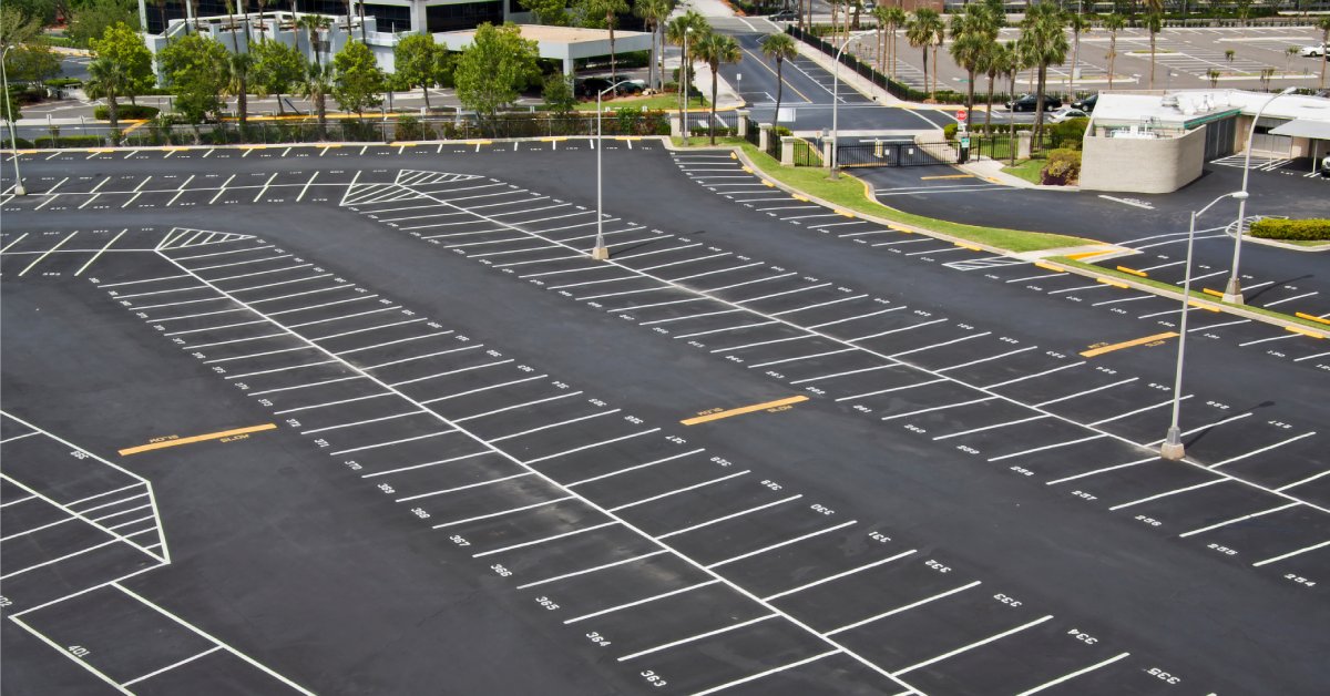 A large, empty parking lot with black asphalt pavement, white lines, and white numbers from an aerial view.