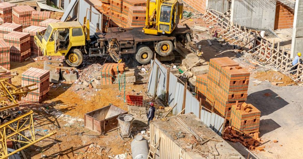 A messy construction site has equipment and materials, including crates and scrap wood, strewn across the site.