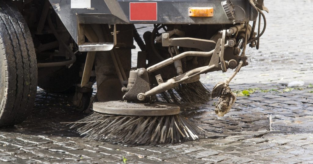 Two round bristle brushes on a street sweeping vehicle spin in circles to clean the black tiled street.