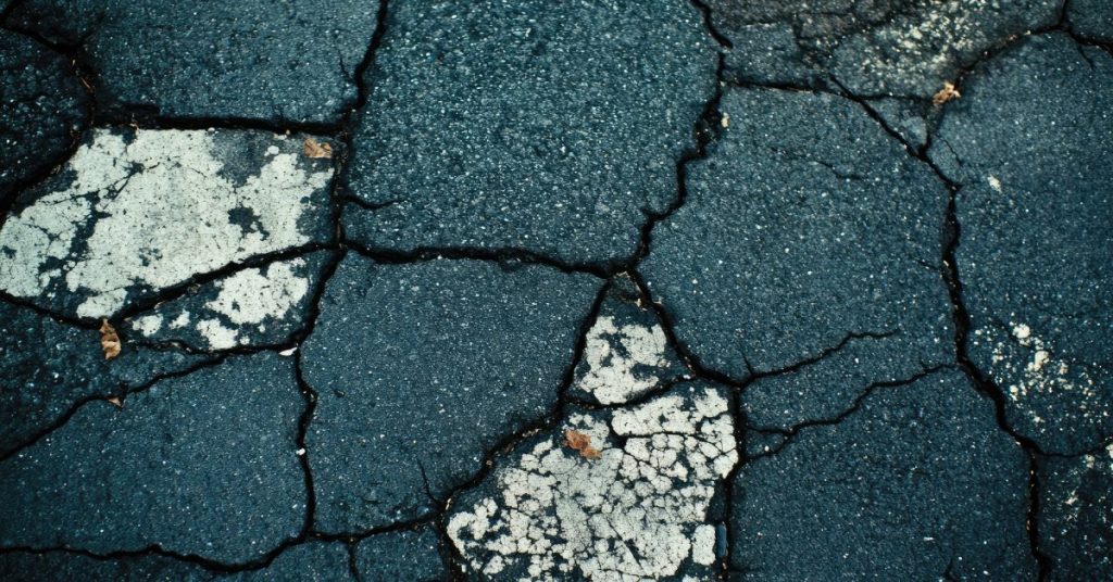 Black asphalt showing several signs of deterioration, including deep circular cracks and white spots.