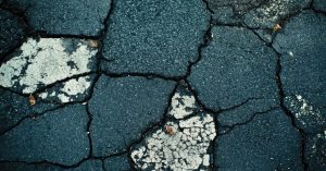 Black asphalt showing several signs of deterioration, including deep circular cracks and white spots.