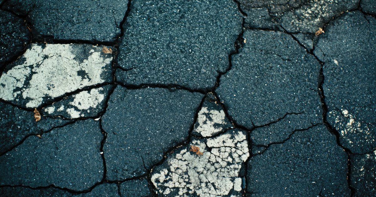Black asphalt showing several signs of deterioration, including deep circular cracks and white spots.
