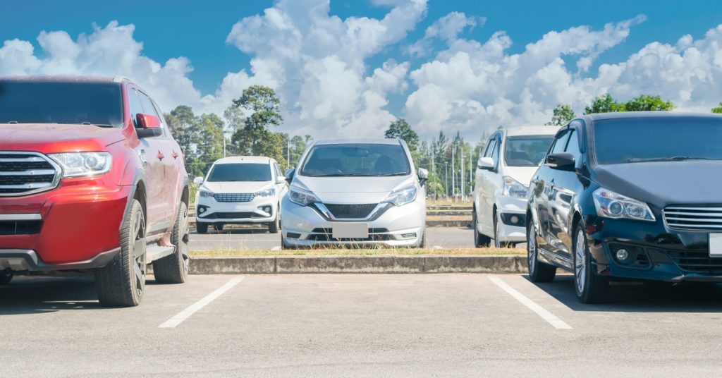An empty spot in a parking lot with gray asphalt sits in between two cars and in front of one other.