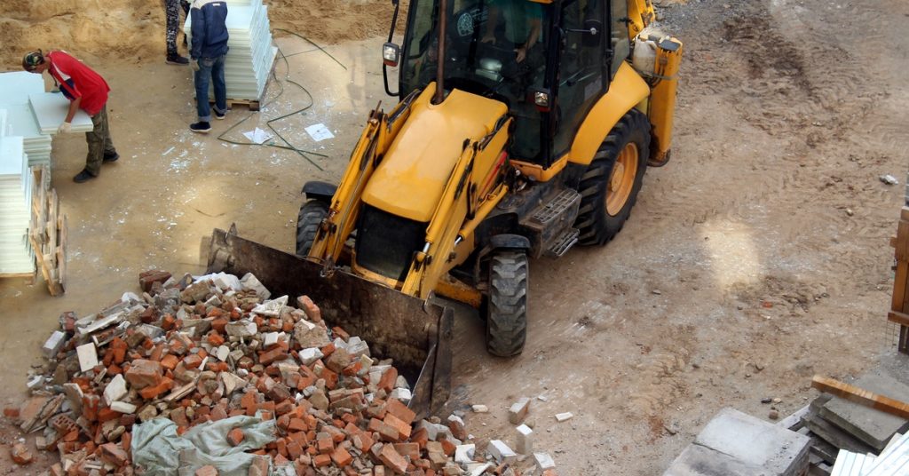 A bulldozer on a construction site pushes a large pile of bricks on the dirt ground with its bucket.