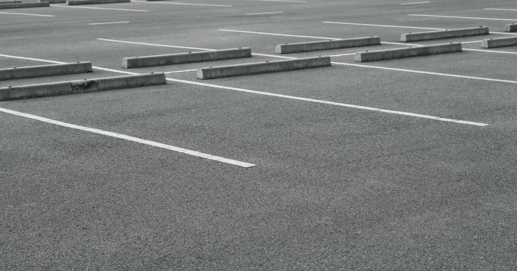 A parking lot with gray pavement, white line striping, and blocks at the end of each spot with no cars in it.