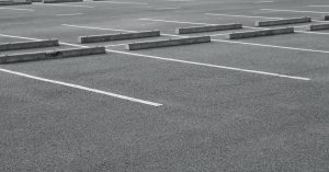 A parking lot with gray pavement, white line striping, and blocks at the end of each spot with no cars in it.