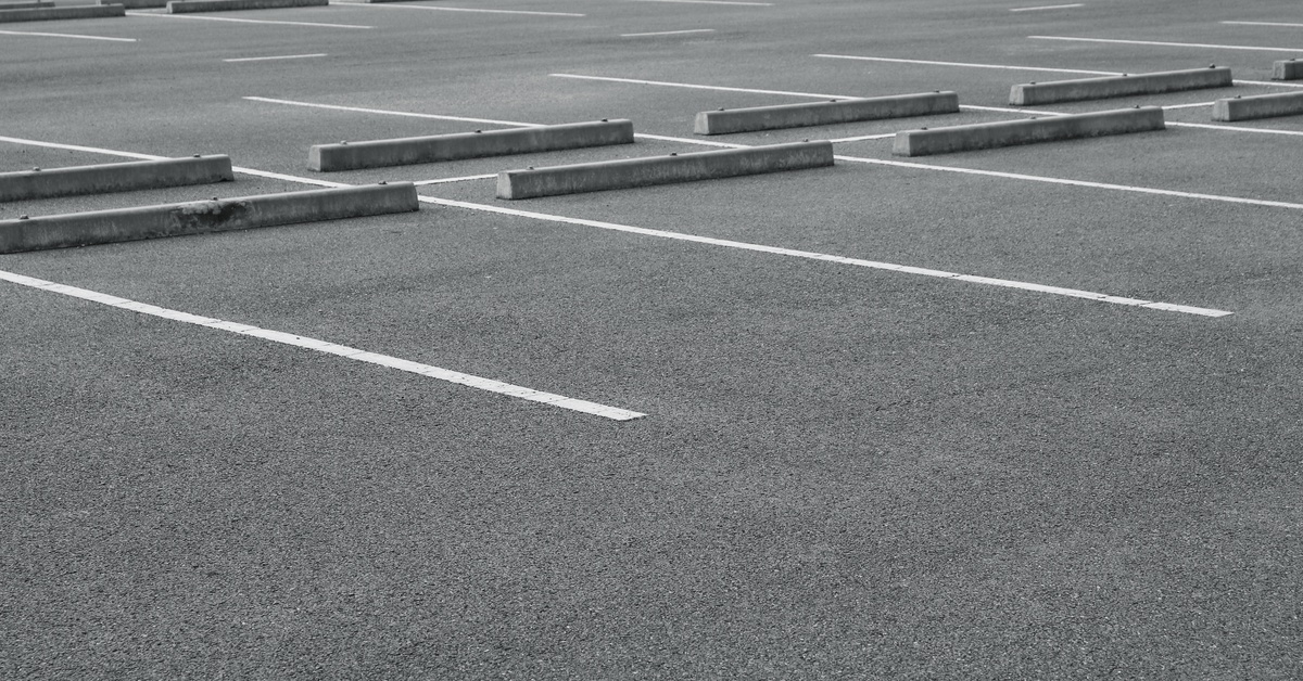 A parking lot with gray pavement, white line striping, and blocks at the end of each spot with no cars in it.