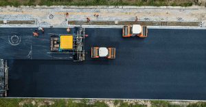 An asphalt paver and two compactors work together to create a smooth black asphalt road.